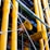 Large yellow industrial pipes are prominently featured, supported by a framework of metal rods and wires. The structure appears to be part of a modern building facade with a mix of exposed pipes and metalwork.