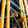 Large yellow industrial pipes are prominently featured, supported by a framework of metal rods and wires. The structure appears to be part of a modern building facade with a mix of exposed pipes and metalwork.