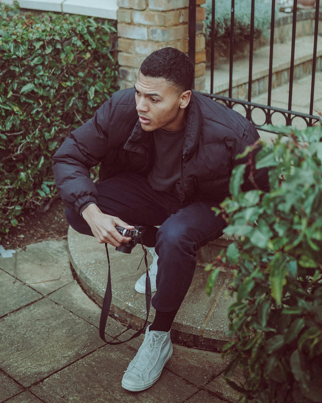 man in black jacket and black pants sitting on black metal fence during daytime