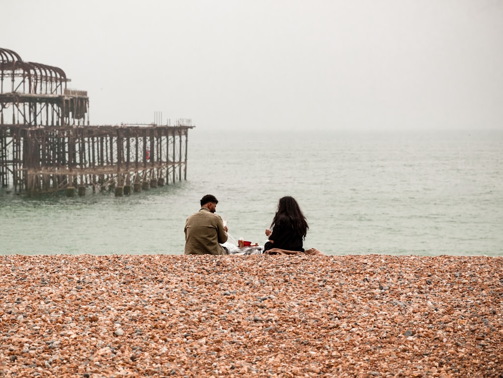 people sitting on brown sand near body of water during daytime