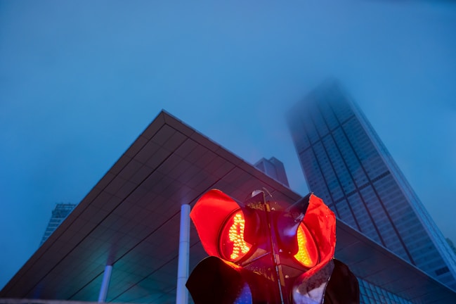A close-up of a glowing signal light piercing through a foggy cityscape at dusk.