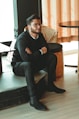 man in black dress shirt sitting on brown chair