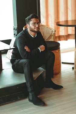 man in black dress shirt sitting on brown chair