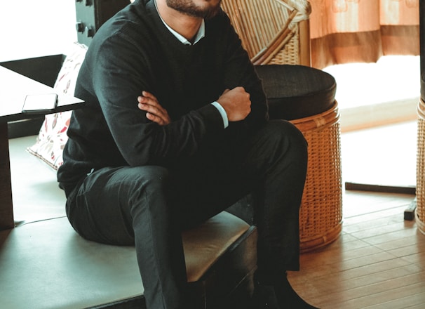 man in black dress shirt sitting on brown chair