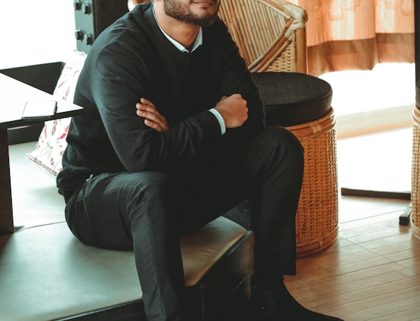 man in black dress shirt sitting on brown chair