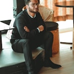 man in black dress shirt sitting on brown chair