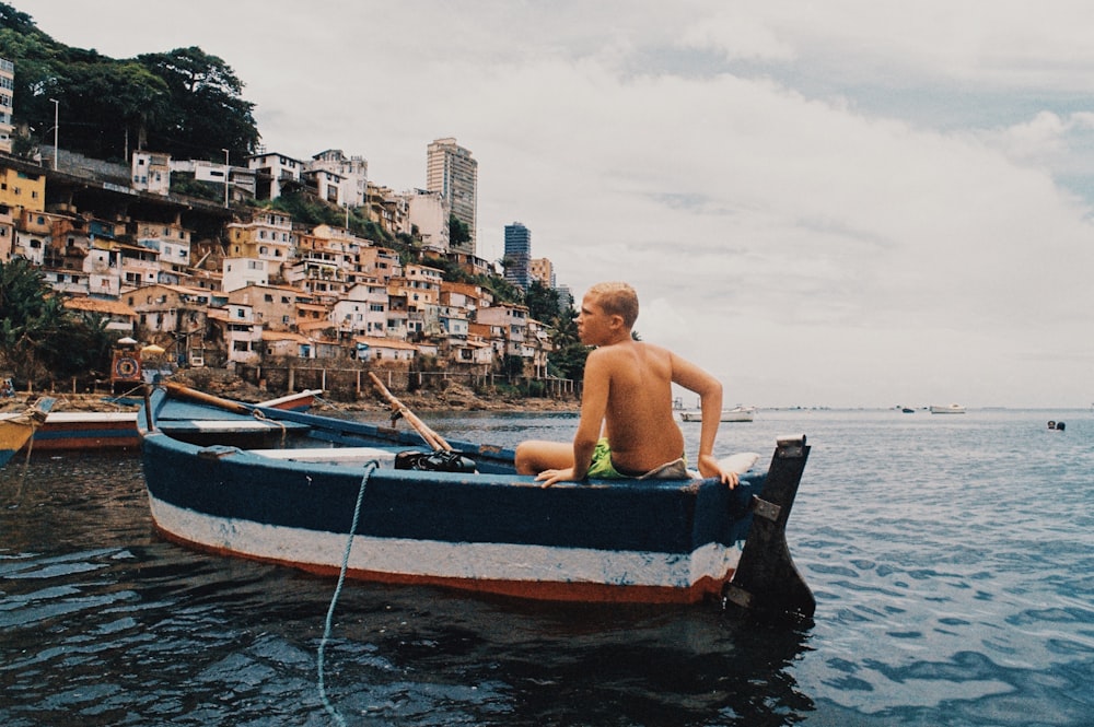 man in blue shorts sitting on brown and blue boat on water during daytime