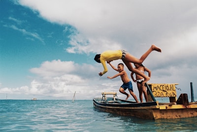 Guests jumping from the boat into clear blue water, surrounded by paddleboards and water toys under a bright tropical sky.