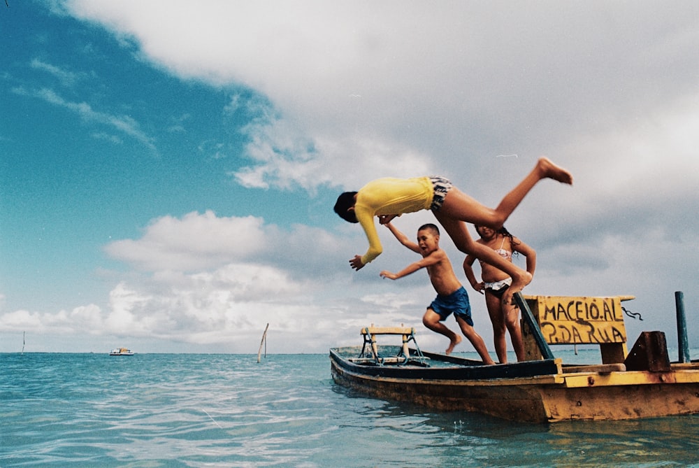 昼間、青い海に浮かぶ茶色の木造船に乗った黄色と青のビキニを着た2人の女性