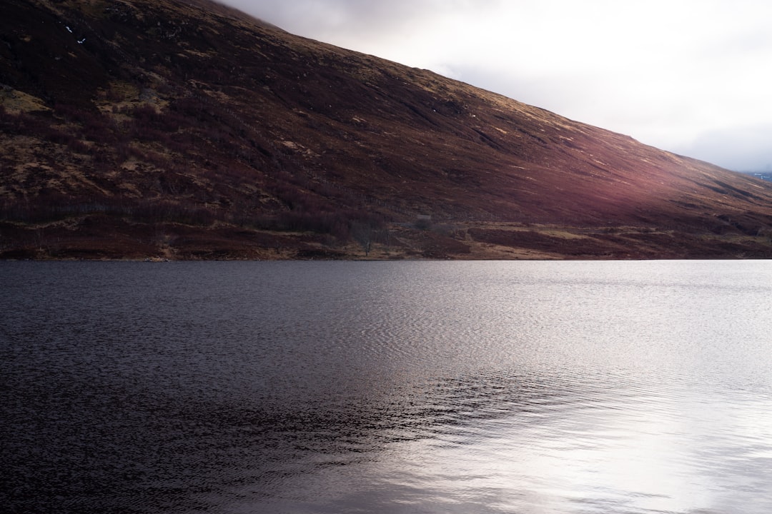 brown mountain beside body of water during daytime