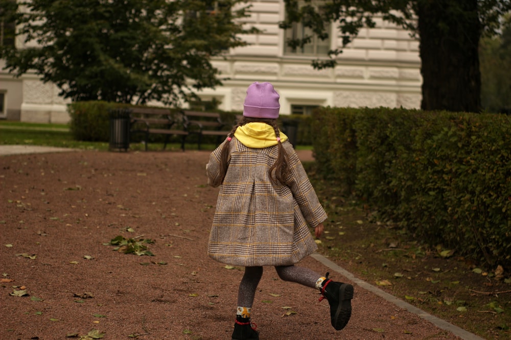 girl in brown coat walking on brown dirt road during daytime