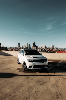 Rear view of a white SUV parked outdoors with city skyline in background.
