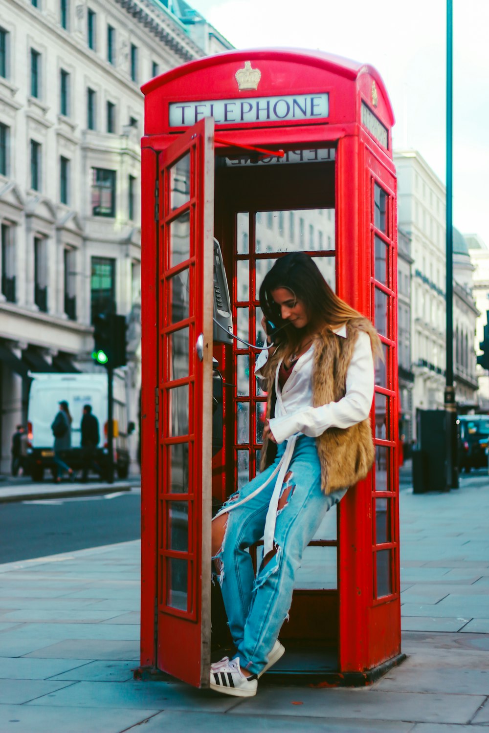 woman in white jacket and blue denim jeans standing on red telephone booth