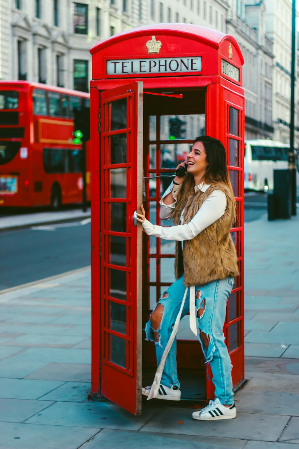 woman in brown long sleeve shirt and blue denim jeans leaning on red telephone booth