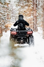 A snowy ATV trail winding through a forest with deer tracks nearby.