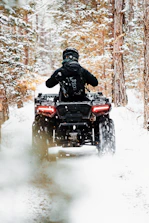 An ATV speeding through a forest trail dusted with fresh snow.