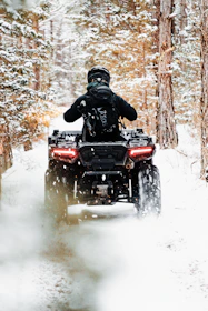 An ATV speeding through a forest trail dusted with fresh snow.