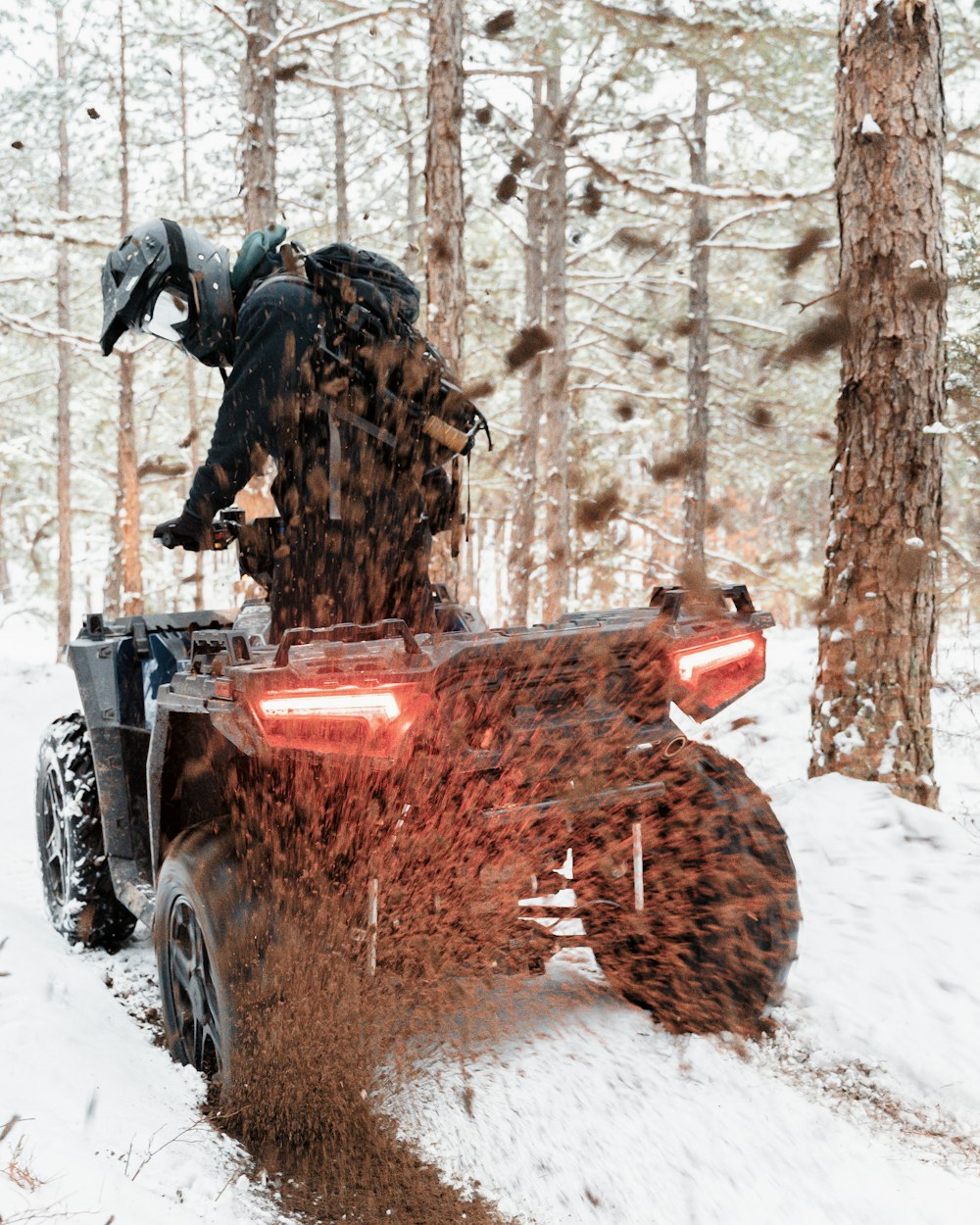 man in black jacket riding on red and black atv on snow covered ground during daytime