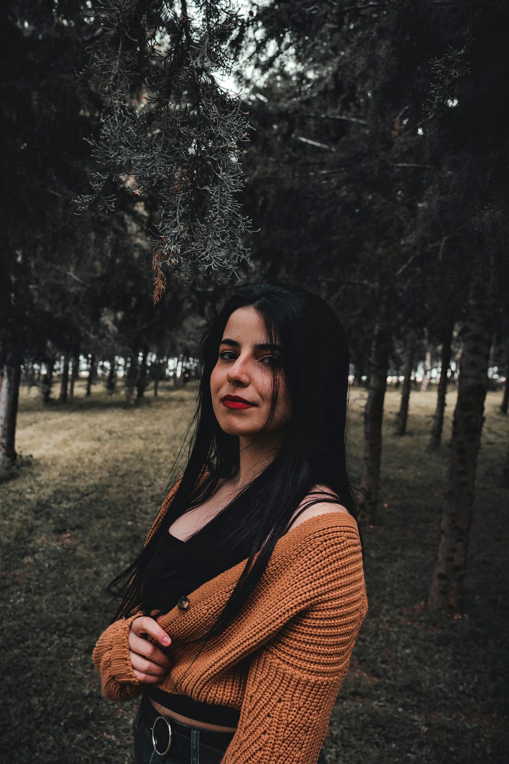 woman in orange knit sweater standing near trees during daytime