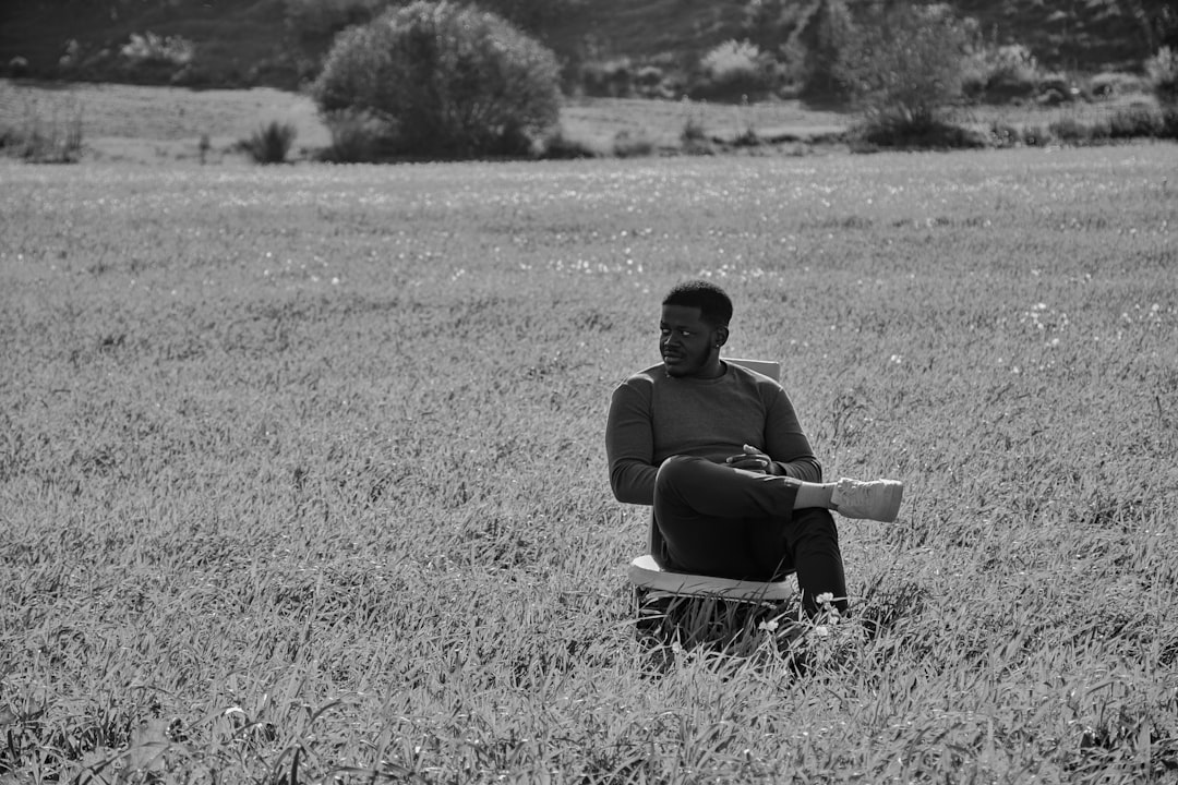 grayscale photo of man sitting on chair on grass field