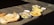 A variety of dishes is spread out on a concrete surface in bright sunlight. The meal includes large crisp papadums, slices of a loaf cake, possibly layered with filling, and what appears to be omelet or scrambled eggs served on oval plates. Small bowls of dipping sauce accompany the dishes.