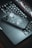 A smartphone with a decorative case lies on top of an open laptop, with the keyboard and a segment of the screen visible. The laptop's screen is displaying a futuristic, abstract interface of charts and curves. The setting has a moody ambience with dim lighting.