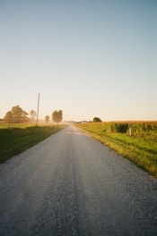 gray asphalt road between green grass field during daytime