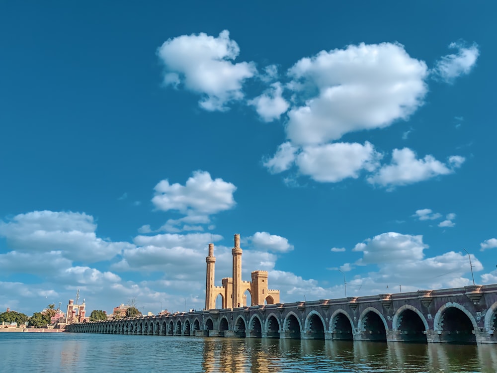 ponte de concreto marrom sobre o corpo de água sob o céu azul e nuvens brancas durante o dia