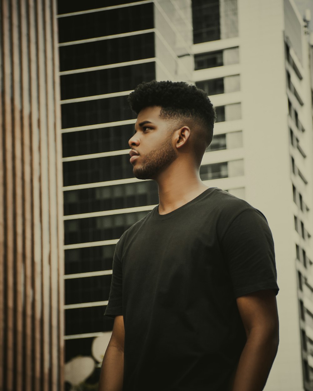 man in black crew neck t-shirt standing near white concrete building during daytime