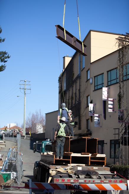 Construction workers installing steel beams on a commercial site under a bright sky.