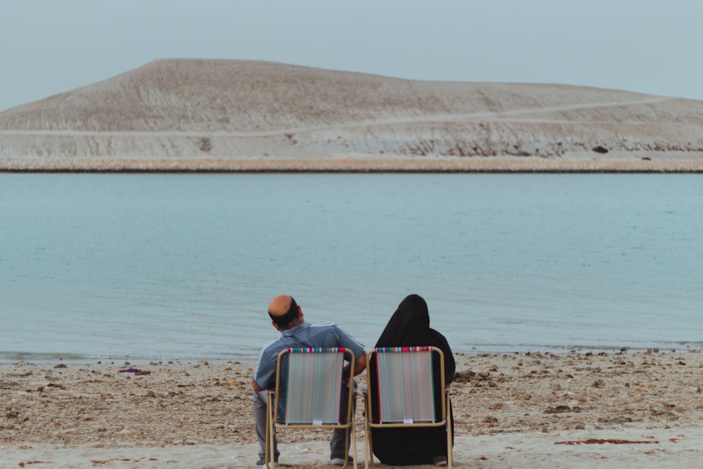 man in black and white striped shirt sitting on chair near body of water during daytime