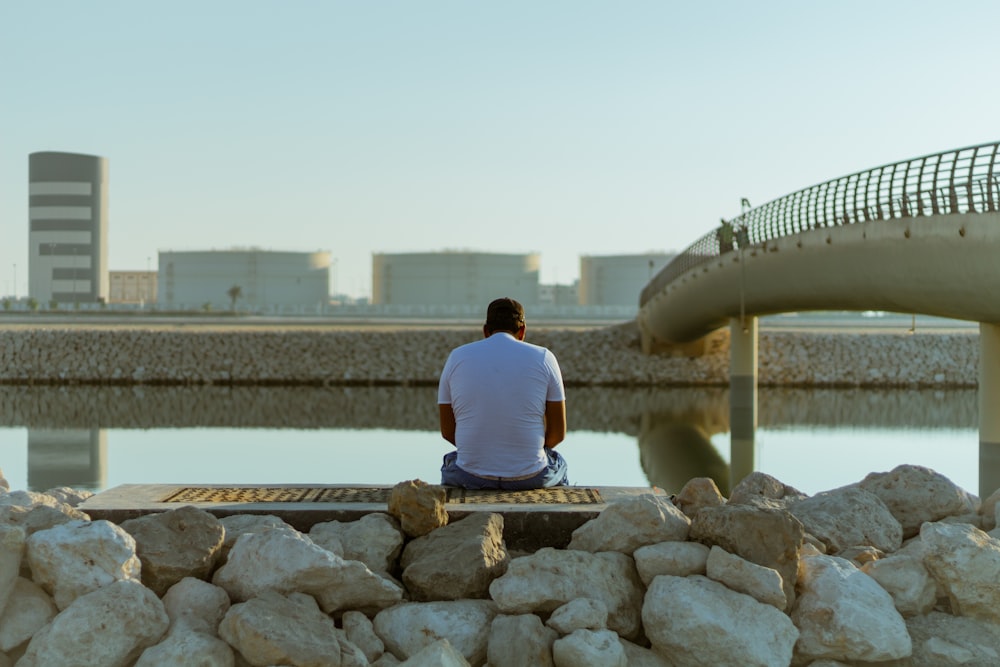 a man sitting on a bench next to a body of water