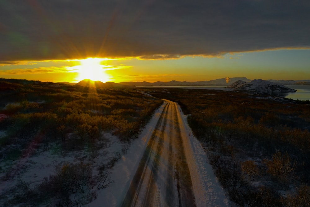 gray road between green grass field during sunset