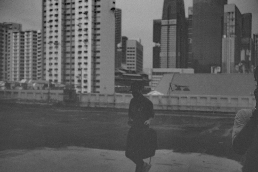 Foto en escala de grises de mujer con abrigo negro caminando por la calle