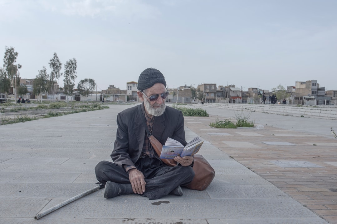 man in black suit jacket sitting on gray concrete bench reading book