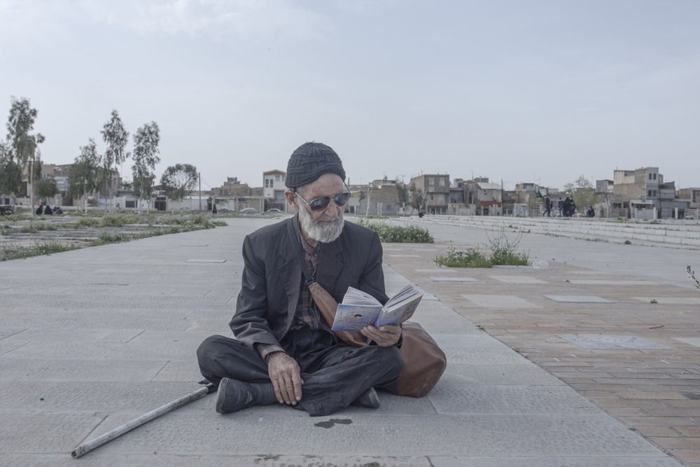 homem na jaqueta do terno preto sentado no banco de concreto cinza lendo o livro