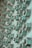 A close-up view of multiple rusted green bolts and nuts attached to a metallic surface, creating a geometric pattern of repeating elements. The bolts show signs of wear and oxidation, contributing to a textured and industrial appearance.