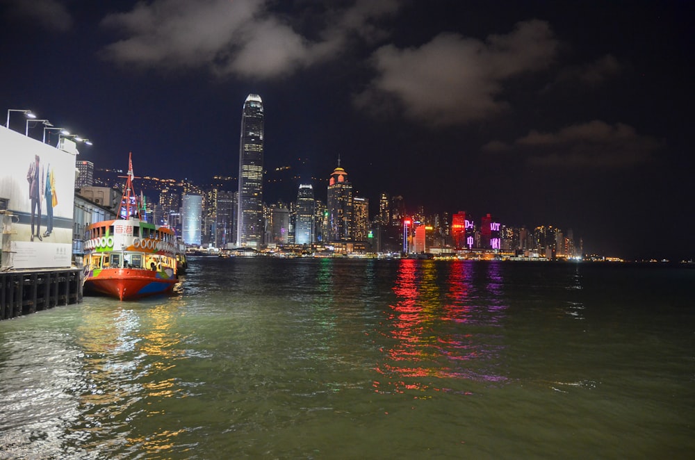 red boat on water near city buildings during night time