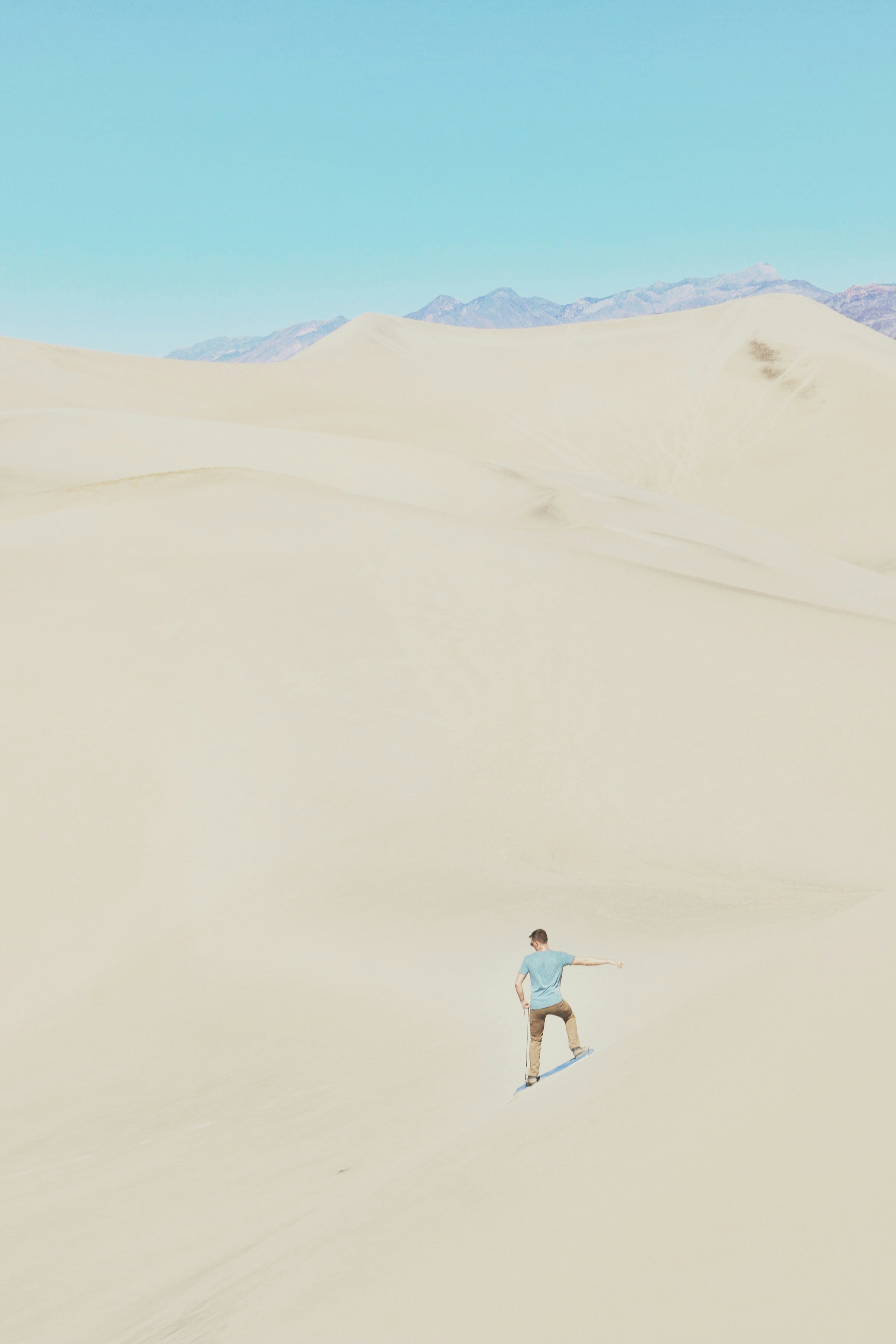 woman in white shirt and blue denim shorts walking on sand during daytime