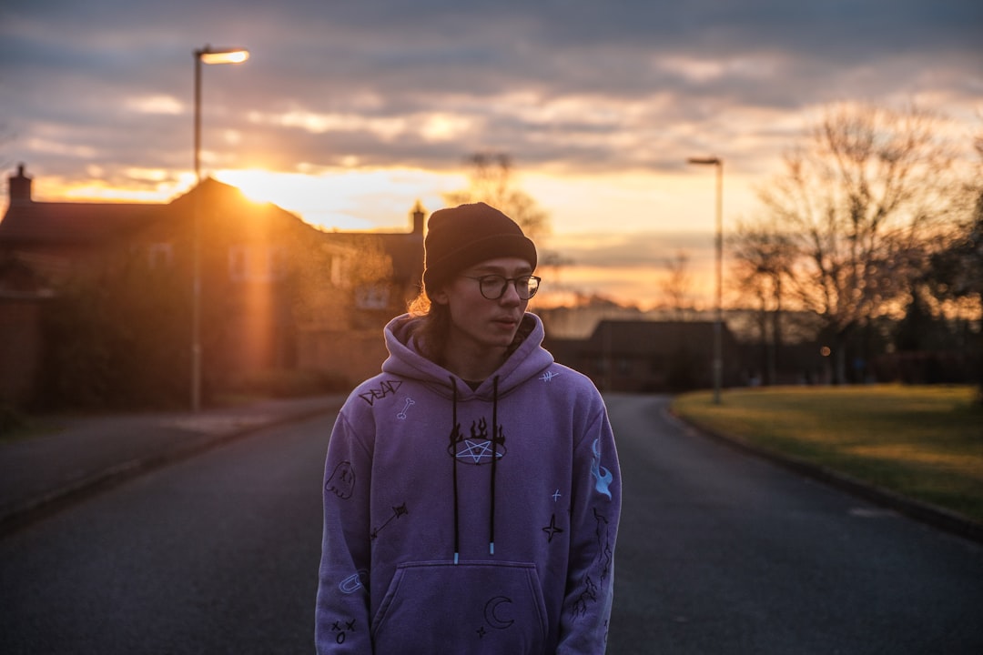 man in gray hoodie standing on road during sunset