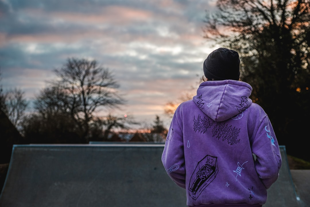 person in purple hoodie standing on road during daytime