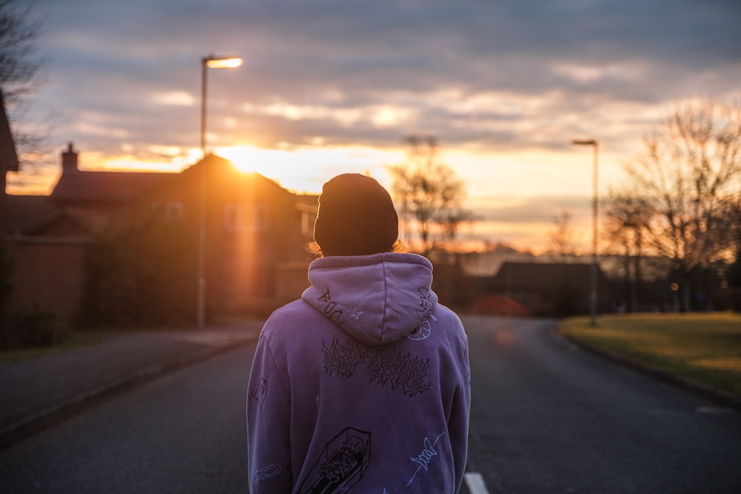 person in gray hoodie standing on road during sunset