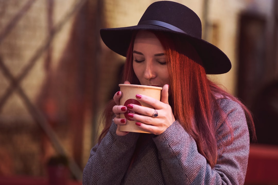 woman in black hat holding white ceramic mug, Cute girl with red hair and hat is drinking thai soup