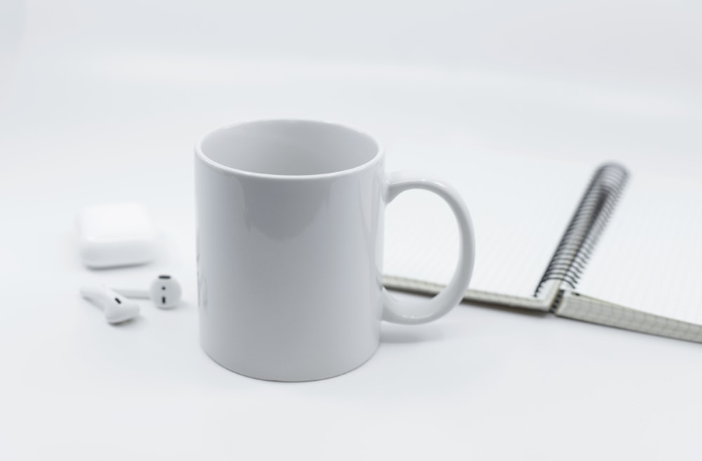white ceramic mug beside white earbuds