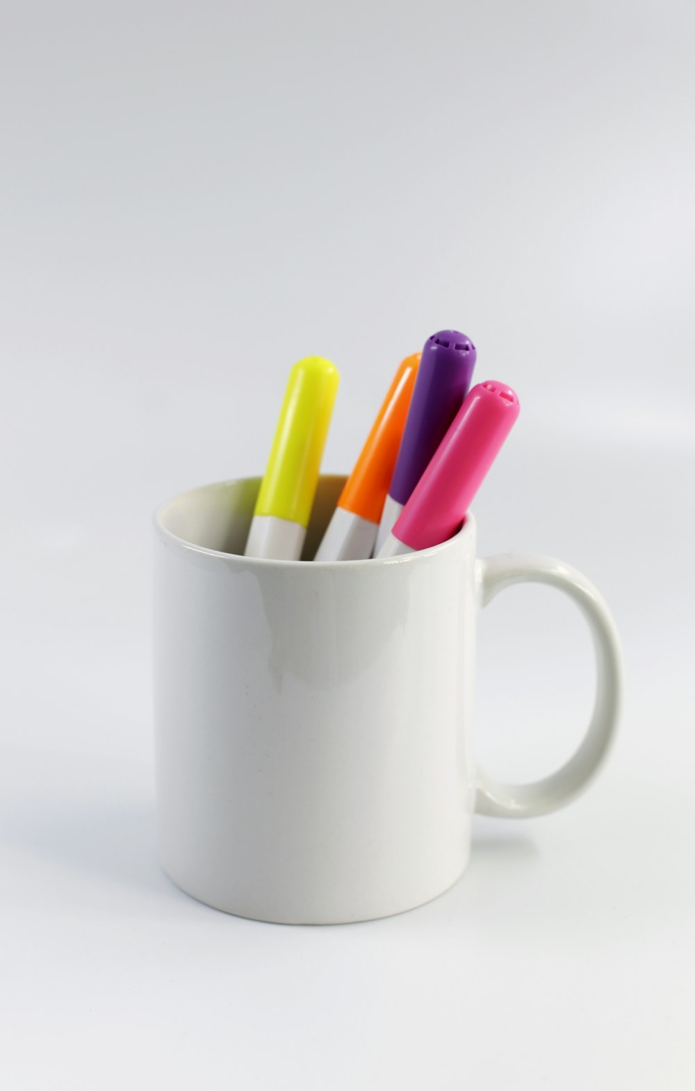 Taza de cerámica blanca con lápices de colores variados