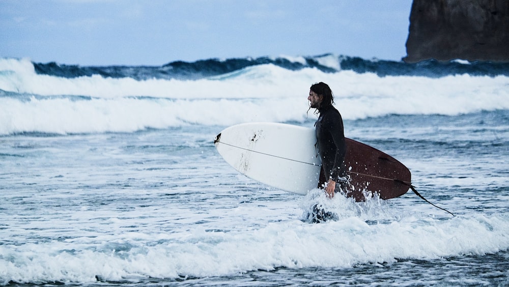 man in black shirt riding on red and white surfboard on sea waves during daytime