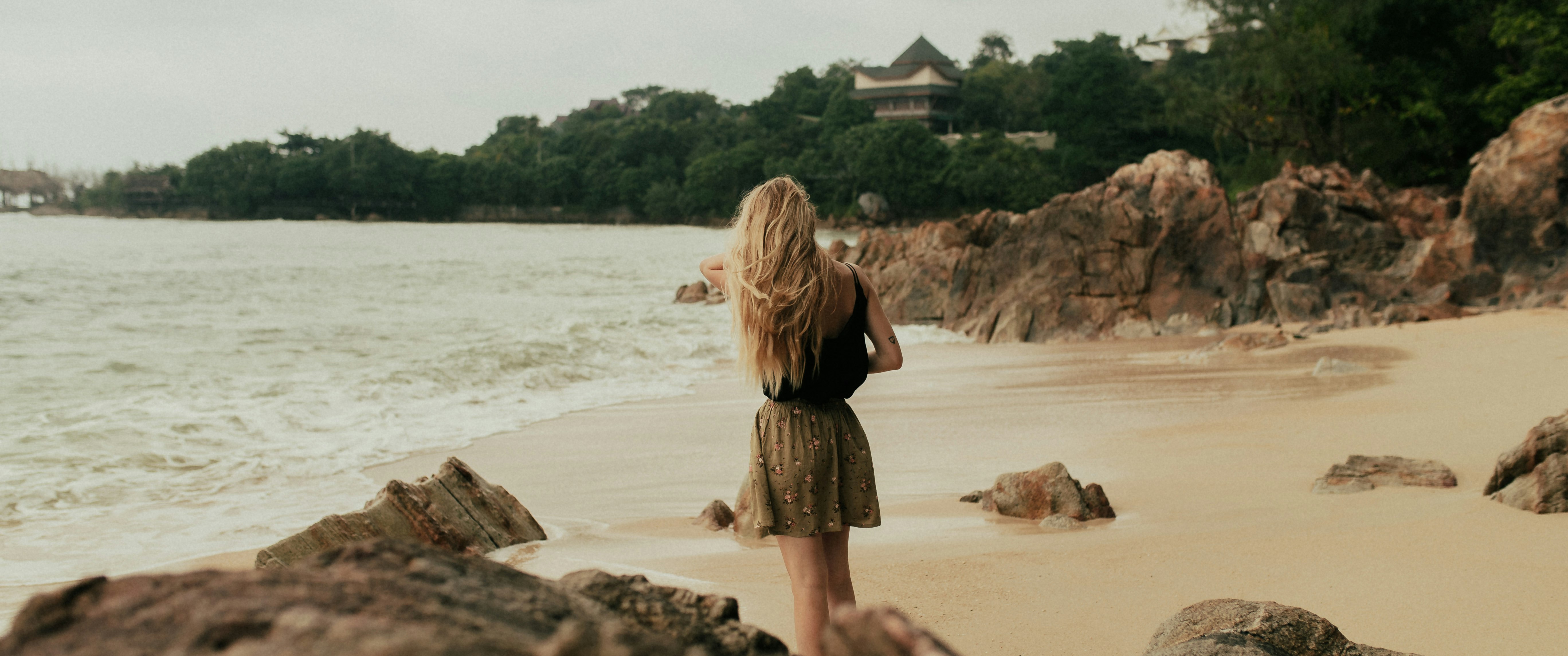 woman in black dress sitting on brown rock near body of water during daytime