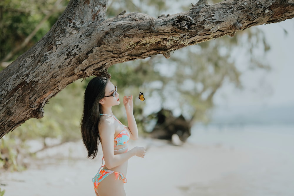 donna in bikini blu e bianco che si appoggia al tronco d'albero marrone durante il giorno