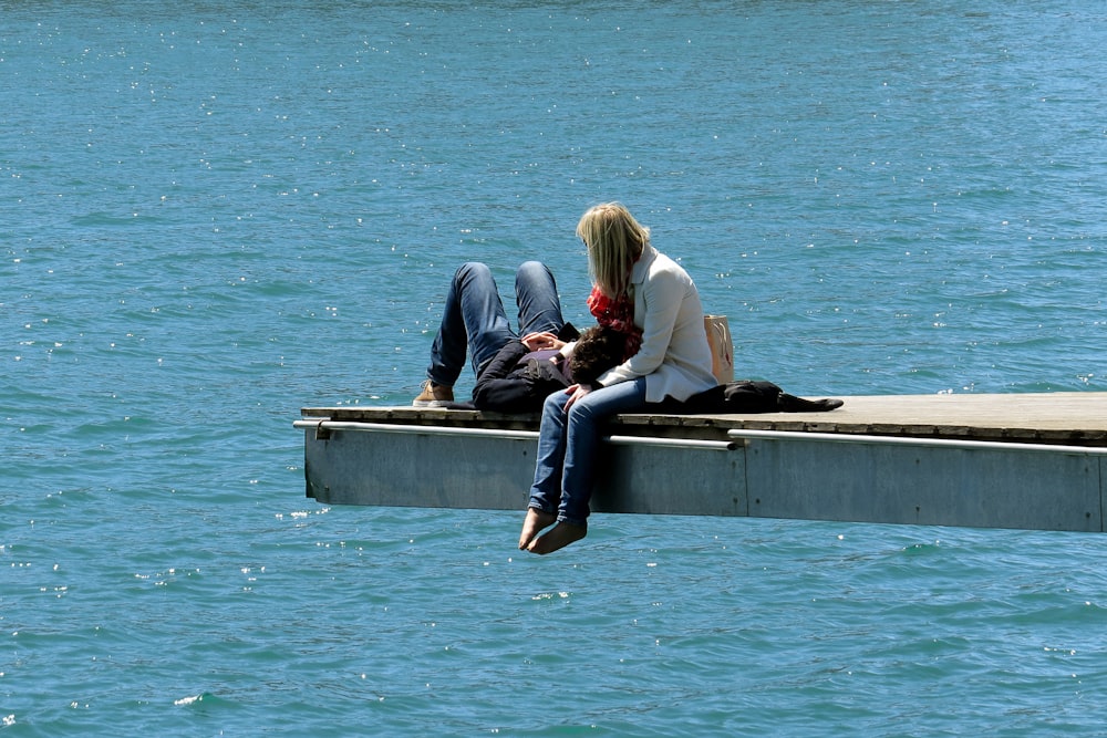 3 women sitting on concrete bench near body of water during daytime