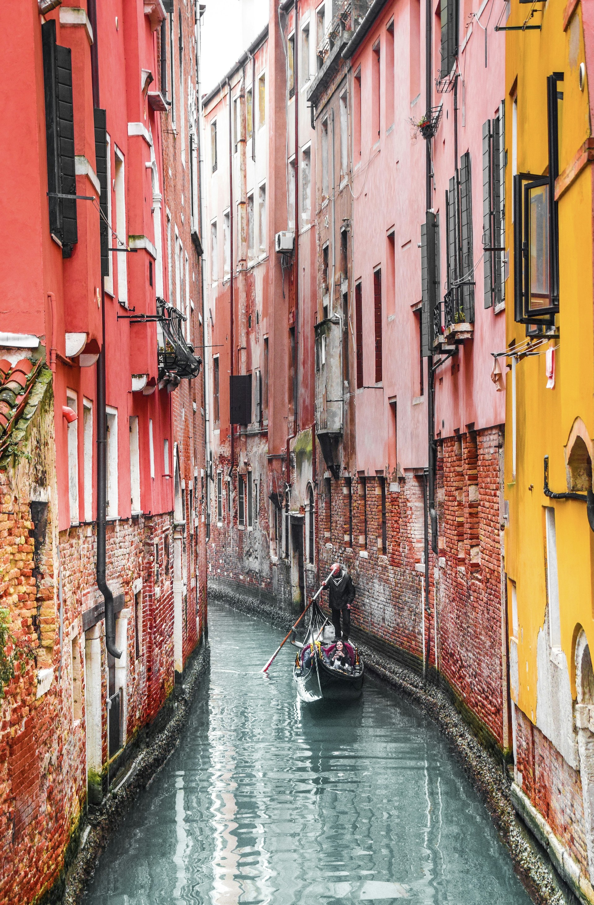 man in black jacket riding on boat on river between red and yellow concrete buildings during